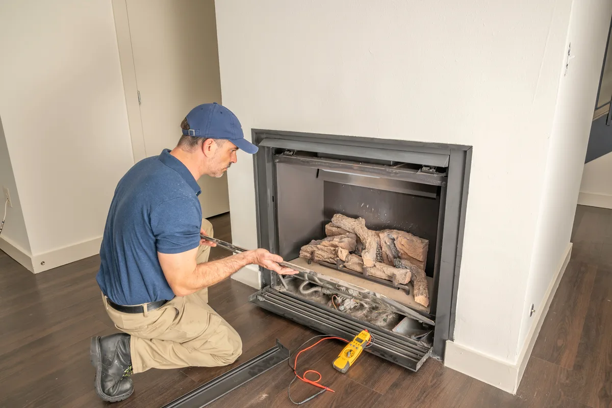 Technician testing a gas fireplace with a multimeter during a repair visit