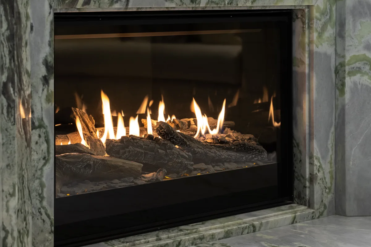 Lit gas fireplace with a ceramic log set in a stone surround