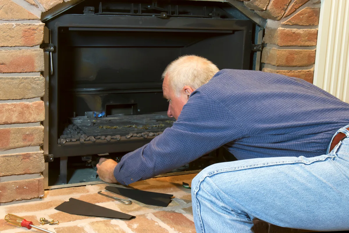 Technician servicing a gas fireplace insert set into a brick surround