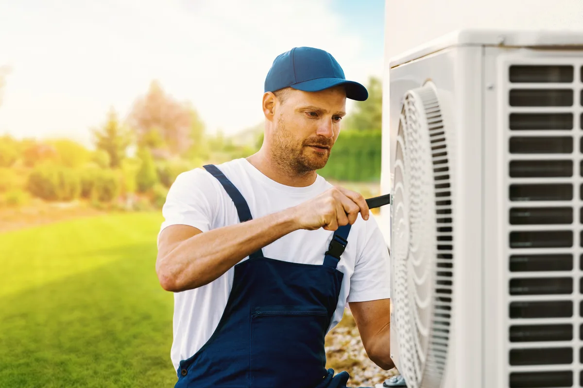 Technician servicing an outdoor heat pump unit during a maintenance visit