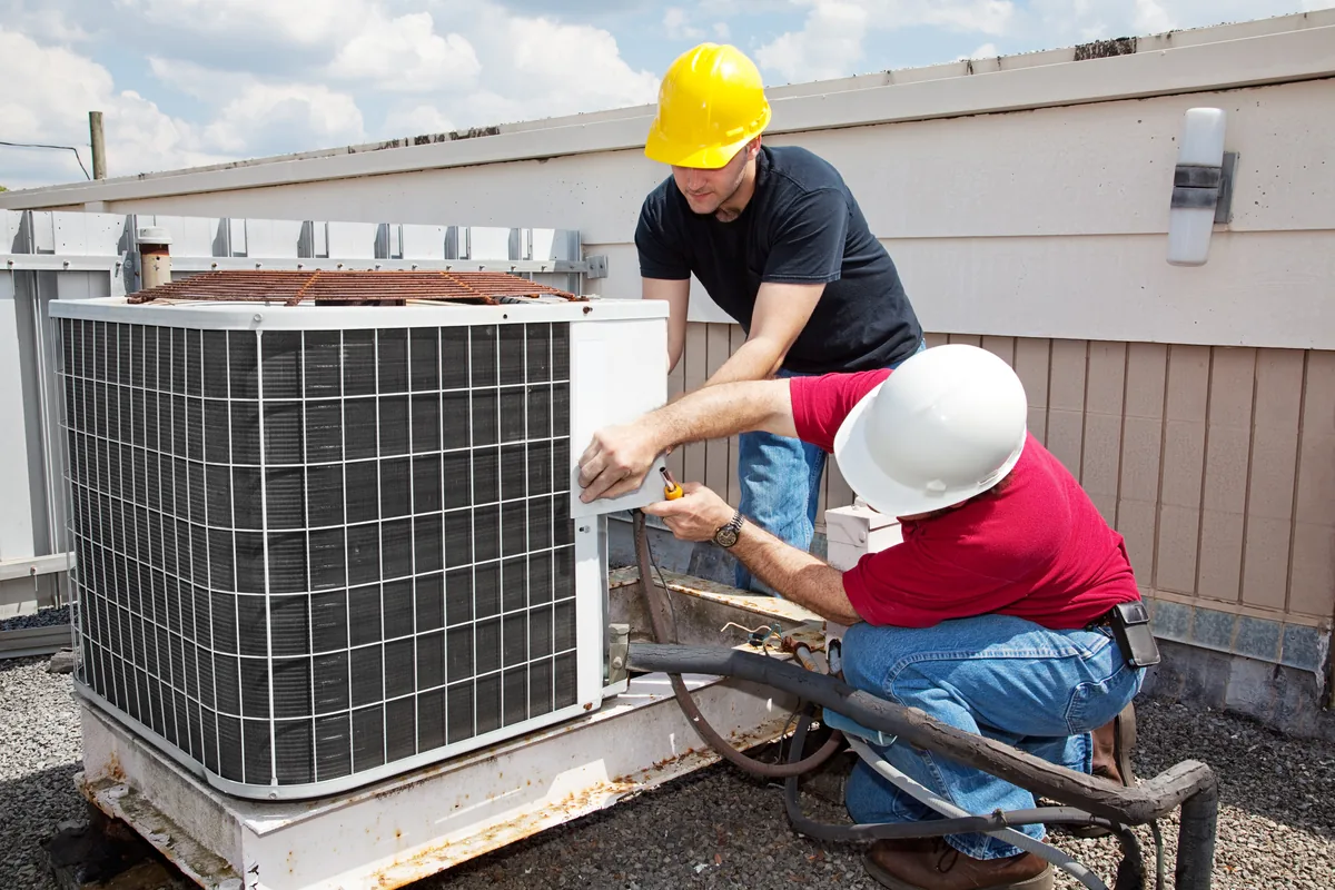 Two HVAC technicians installing an outdoor condensing unit