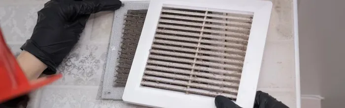 Technician fitting a return-air filter behind a wall register